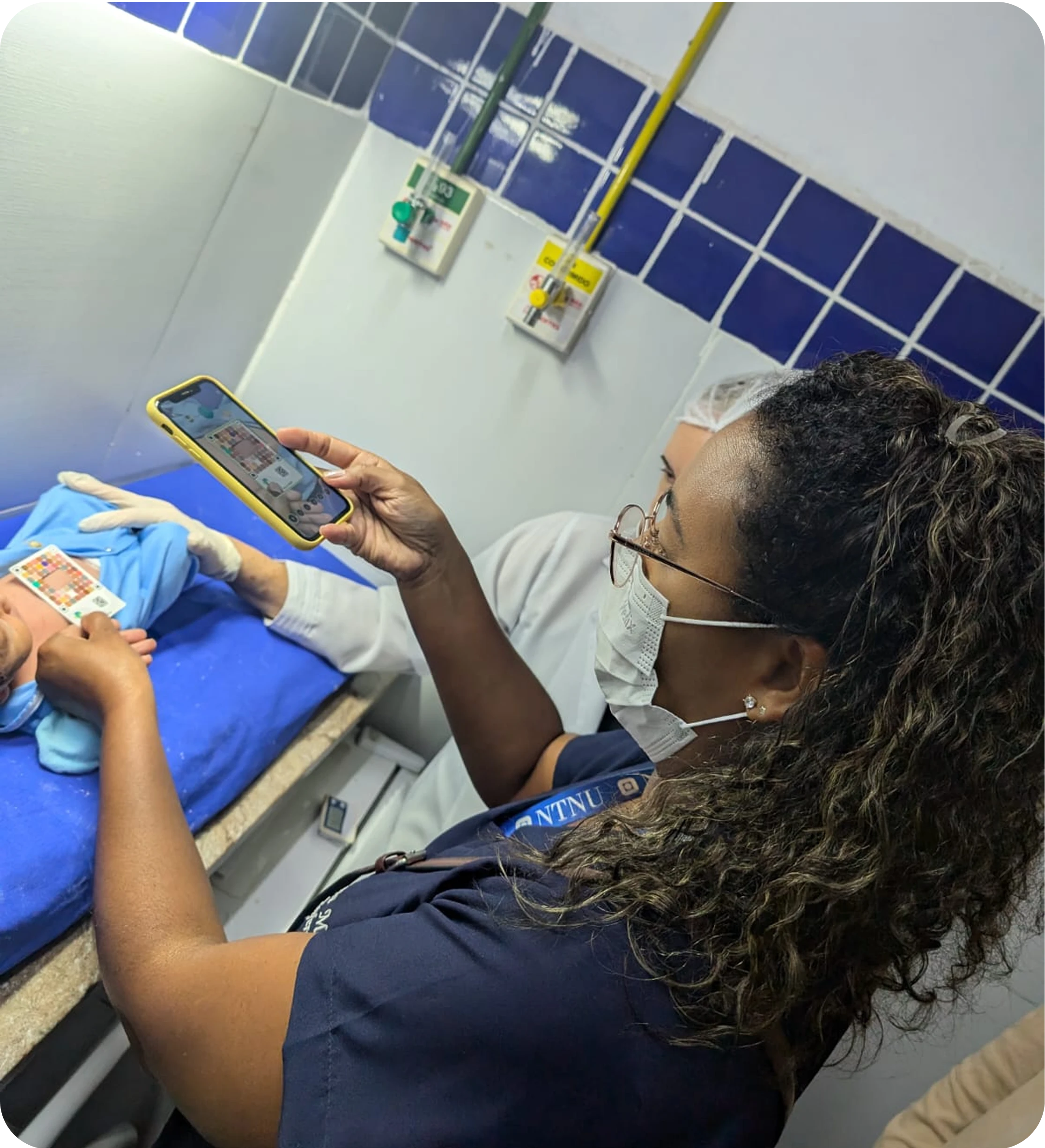 Healthcare worker using the Picterus app to scan a newborn with a calibration card on a blue exam table.